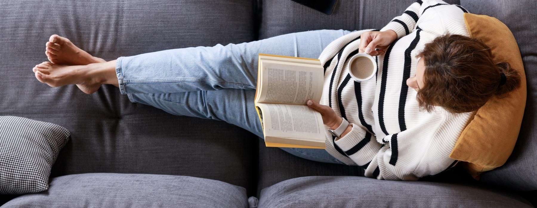 a person lying on a couch reading a book
