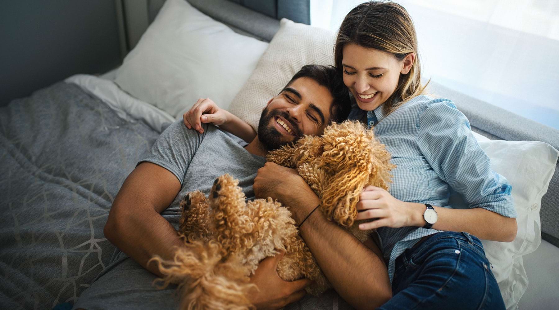 Welcome Home couple laying in bed with family dog